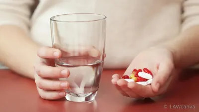Frau hält Wasserglas in der rechten Hand und in der linken Hand verschiedene Tabletten und Kapseln Medikamente helfen nur, wenn sie richtig eingenommen werden