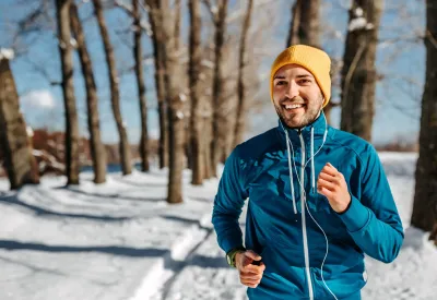 Ein Mann joggt durch einen verschneiten Wald. Sport kann im Winter das Immunsystem stärken. Fit durch den Winter