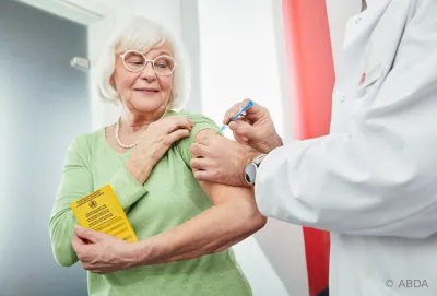 Seniorin mit Impfbuch in der Hand wird von Apotheker geimpft Grippeschutz jetzt auffrischen – schützt mich und andere