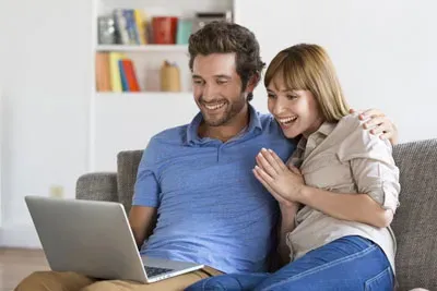 Zwei junge Menschen freuen sich am Laptop – vermutlich über gefundenen echten Schungit. Wer sind diese Menschen, die Schungit kaufen?